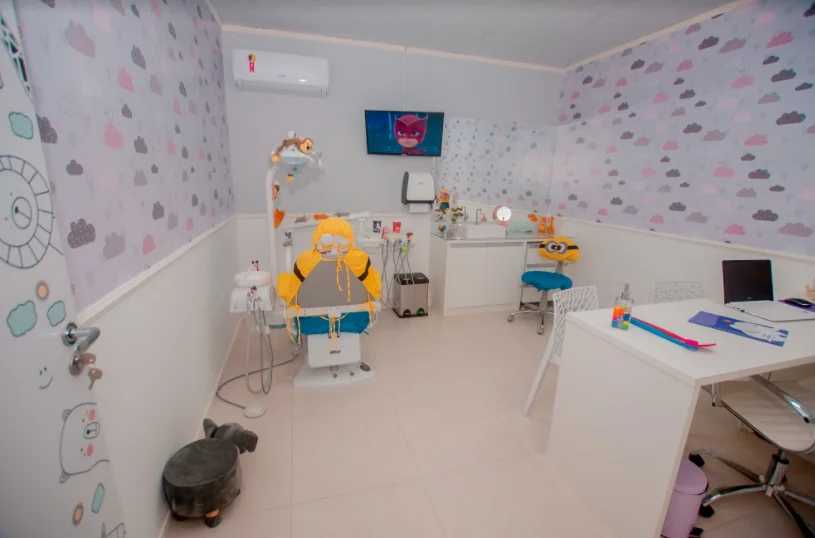 Consultório infantil com cadeira amarela, papel de parede de nuvens e bancada